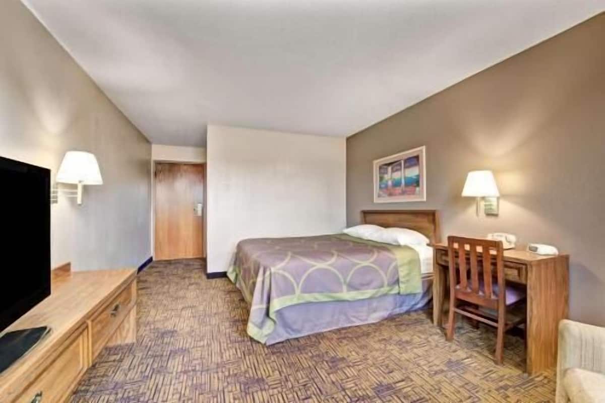A hotel room with a bed, a desk, a chair, a television, and a painting on the wall.