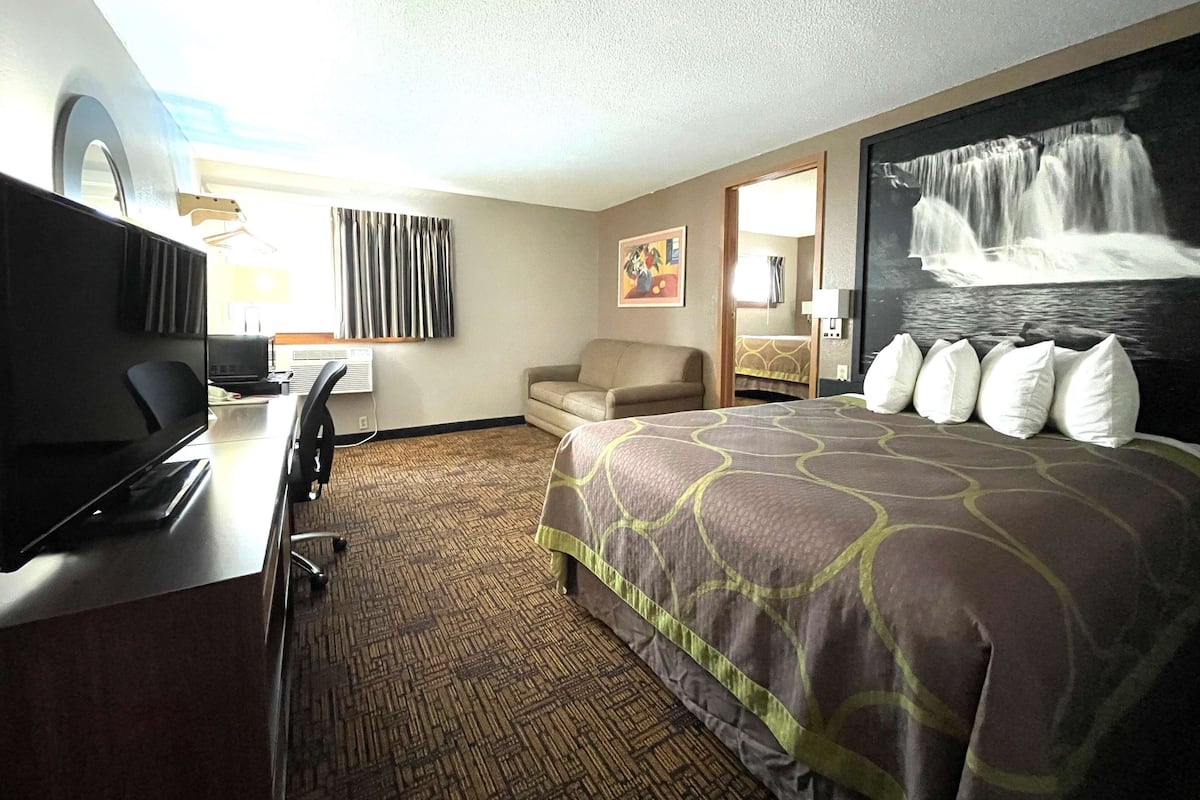 A hotel room with a bed, a desk with a computer, a chair, a TV, and a painting of a waterfall.