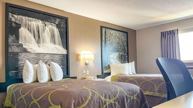 A hotel room with two beds, a desk, and a chair. There are large framed pictures on the walls.