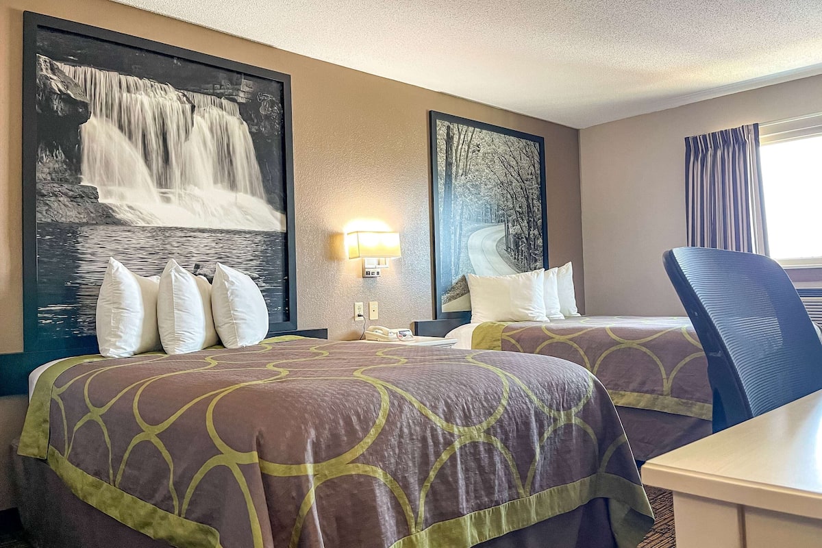 A hotel room with two beds, a desk, and a chair. There are large framed pictures on the walls.