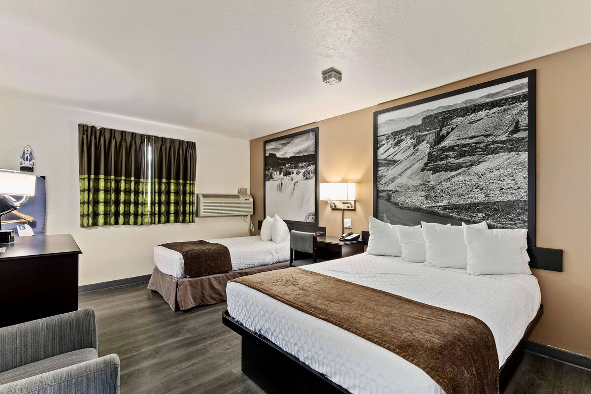 Hotellihuone, jossa on kaksi sänkyä, työpöytä, tuoli ja suuri maisemamaalaus seinällä.