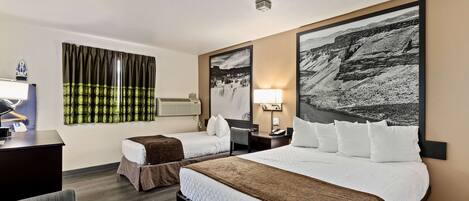 A hotel room with two beds, a desk, a chair, and a large landscape painting on the wall.