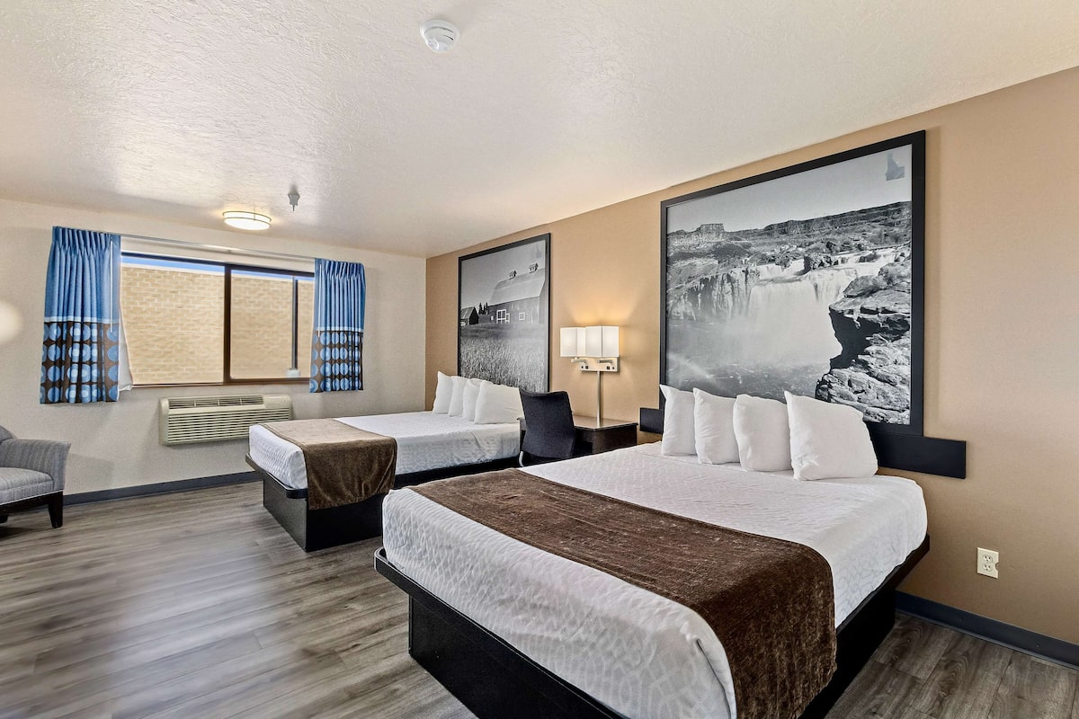 Hotellihuone, jossa on kaksi sänkyä, tuoli, työpöytä ja suuri kehystetty taulu seinällä.