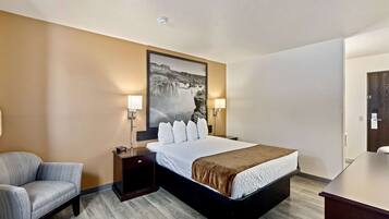 Habitación de hotel con cama, una silla, un escritorio y un cuadro grande en la pared.
