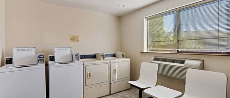 A laundry room with two washers and dryers, a bench, and a window with blinds.
