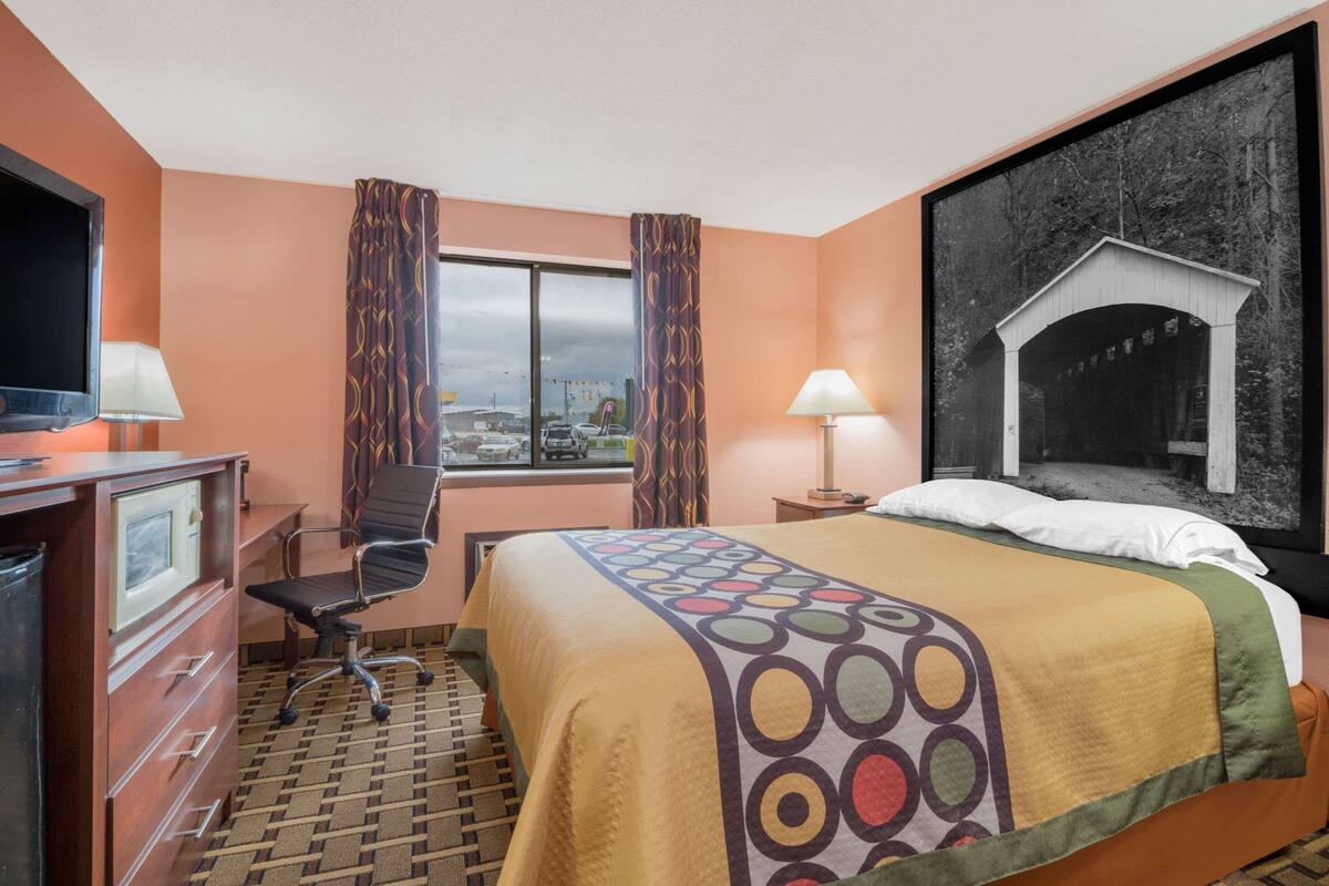 Een hotelkamer met een bed, bureau, stoel, televisie en een groot raam met gordijnen.