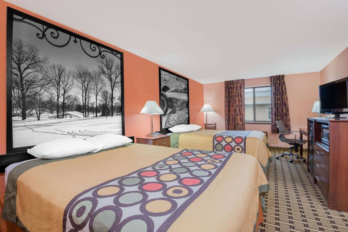 Een hotelkamer met twee bedden, een bureau, een televisie en een groot raam met gordijnen.