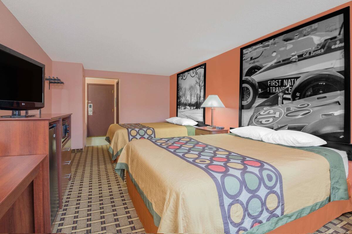 Een hotelkamer met twee bedden, een televisie, een bureau en een lijst met een afbeelding van een raceauto.