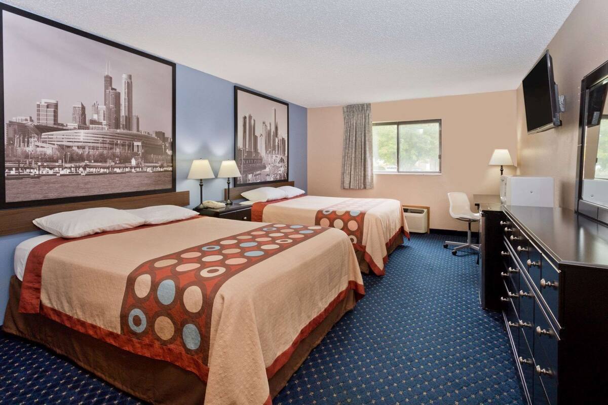 Habitación de hotel con dos camas, un escritorio, un televisor y fotografías de la ciudad en la pared.