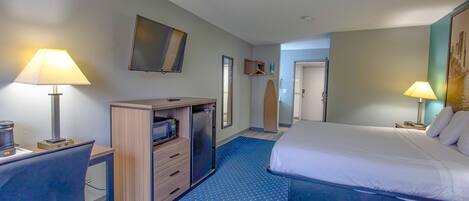 Quarto de hotel com cama, escrivaninha e cómoda. Há uma televisão na parede e um quadro sobre a cama.