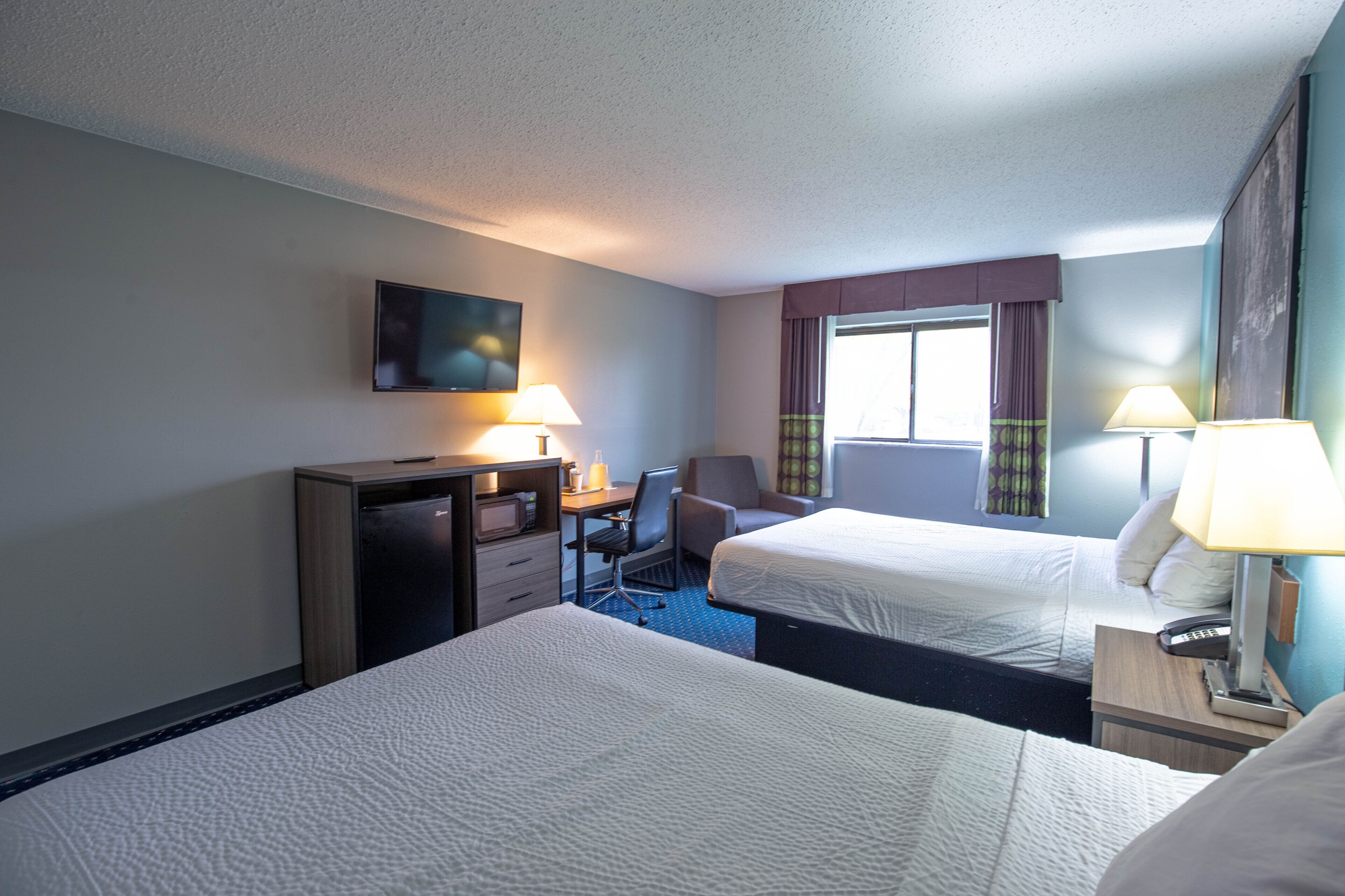 A hotel room with two beds, a desk, a chair, a TV, and a window with curtains.