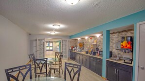 A modern kitchen with dark cabinets, a glass dining table, and a brick accent wall. - Super 8 by Wyndham Rockford I-90/Casino District (Rockford)