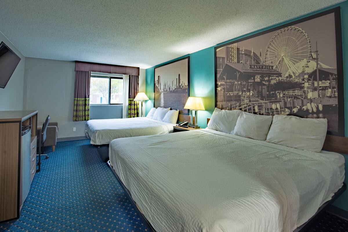 Habitación de hotel con dos camas, un escritorio y un gran mural de la ciudad en la pared.