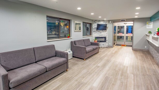 A modern waiting area with two grey sofas, a flat-screen TV mounted on the wall, and a reception desk with a plant. - Super 8 by Wyndham Rockford I-90/Casino District (Rockford)
