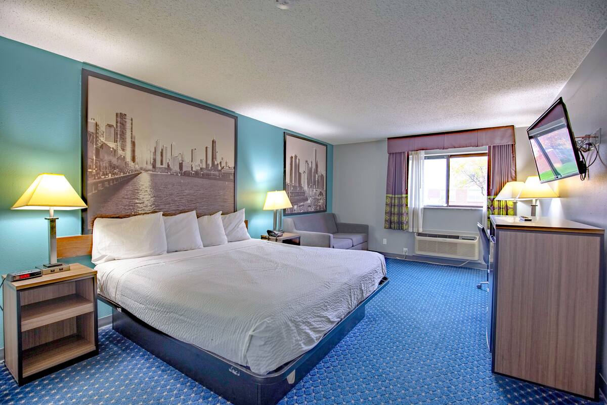 Habitación de hotel con una cama grande, dos mesitas de noche con lámparas, un escritorio, una silla y un ventanal con cortinas.