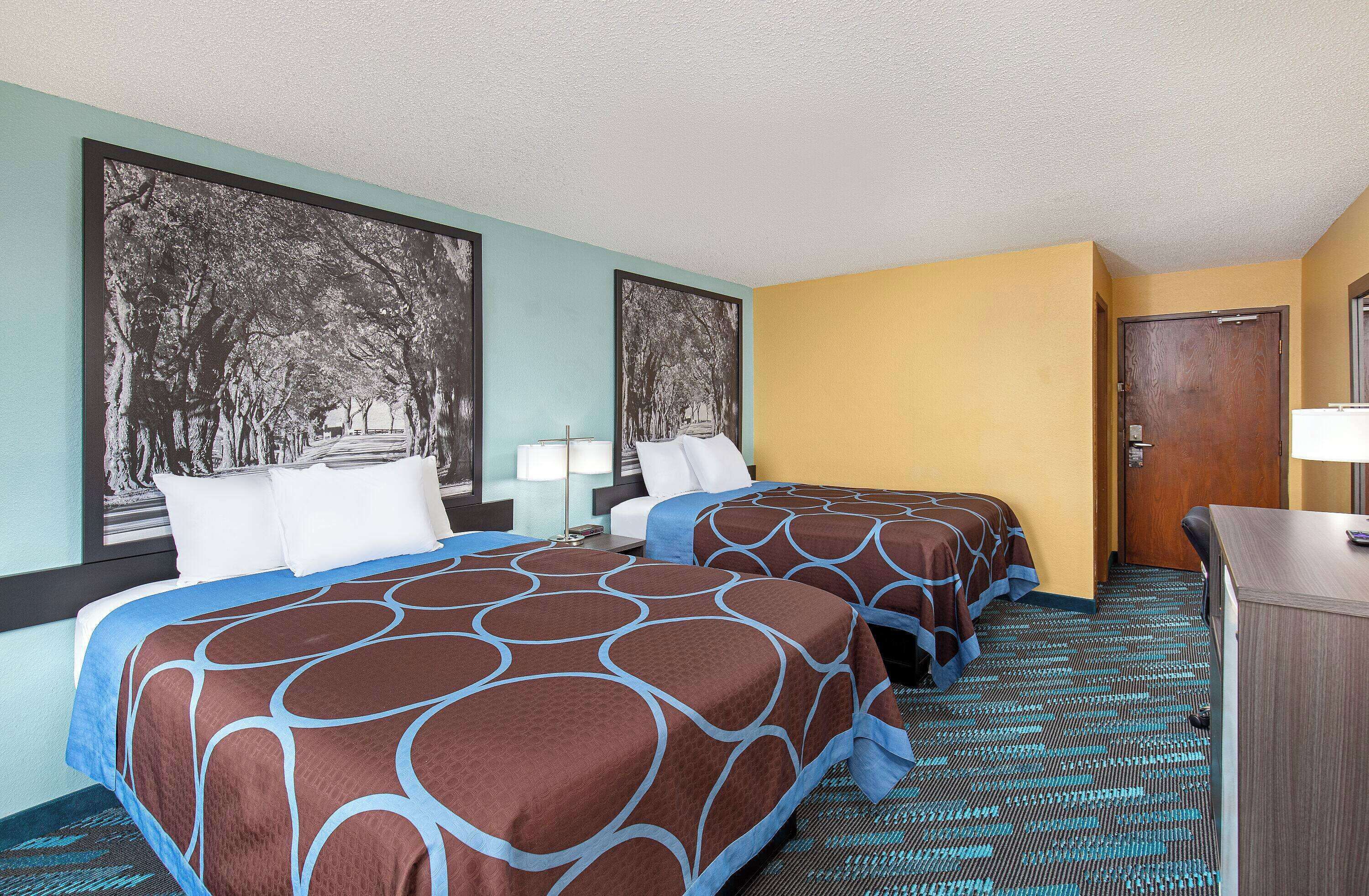 A hotel room with two beds, a desk, and a door.