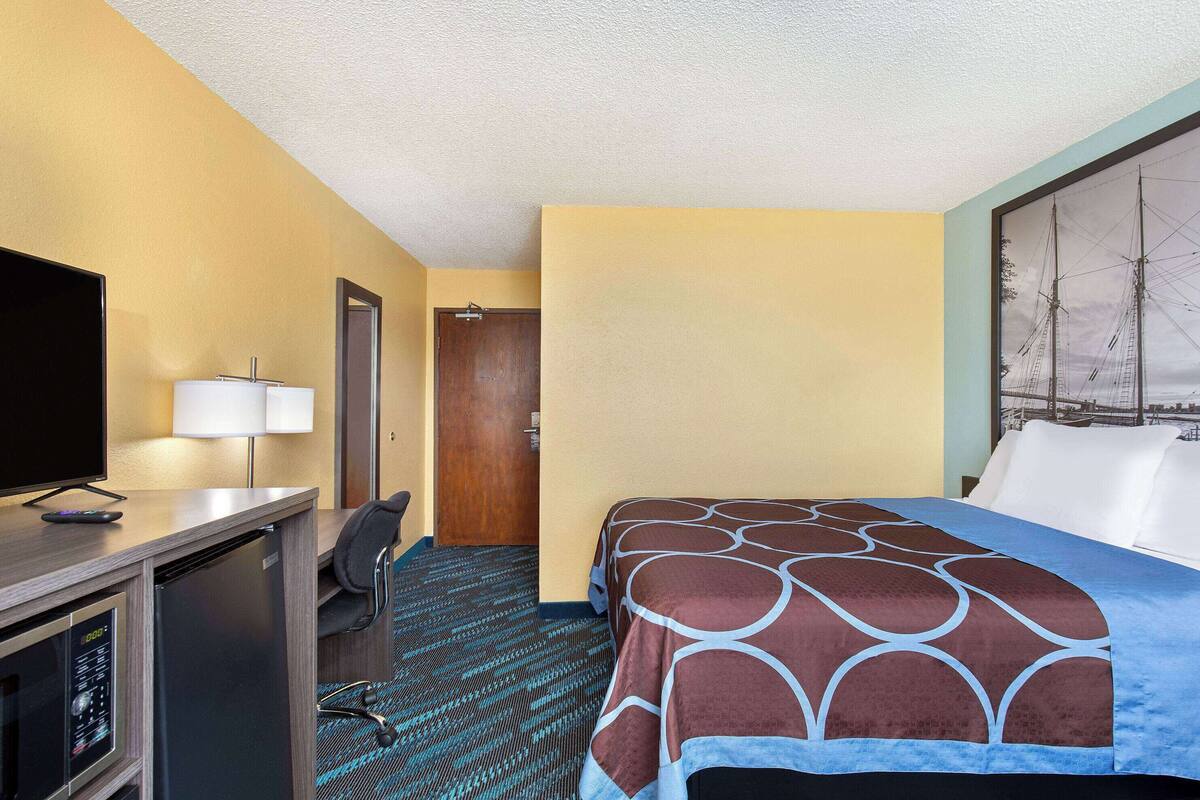 Una habitación de hotel con cama, escritorio con televisor, lámpara y puerta.