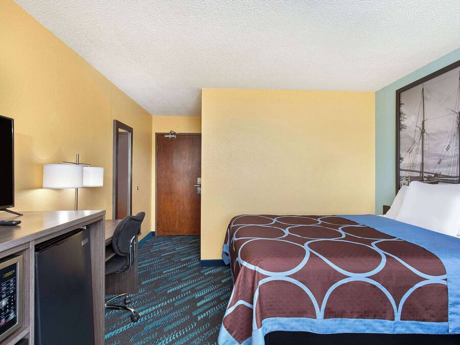 Una habitación de hotel con cama, escritorio con televisor, lámpara y puerta.