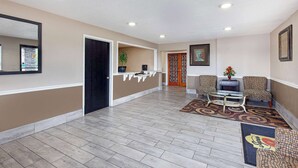 A reception area with a reception desk, two patterned armchairs, a coffee table, a potted plant, and a framed picture on the wall. - Super 8 by Wyndham Somerset (Somerset)