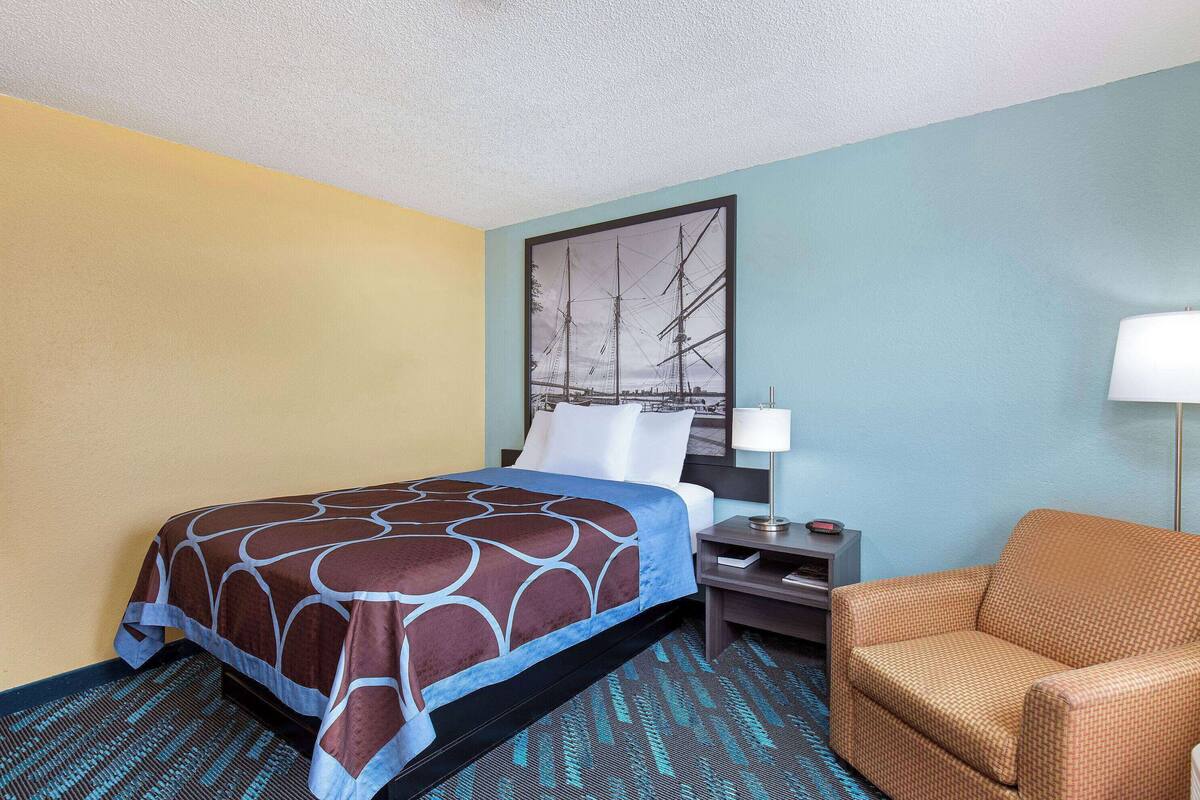 Una habitación de hotel con cama, mesita de noche, lámpara y una silla.