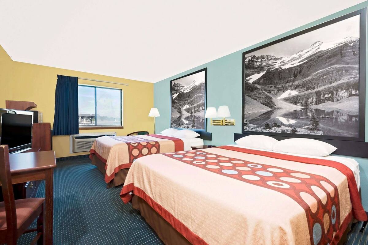 Habitación de hotel con dos camas, un escritorio, televisión y grandes ventanales con vistas a la montaña.