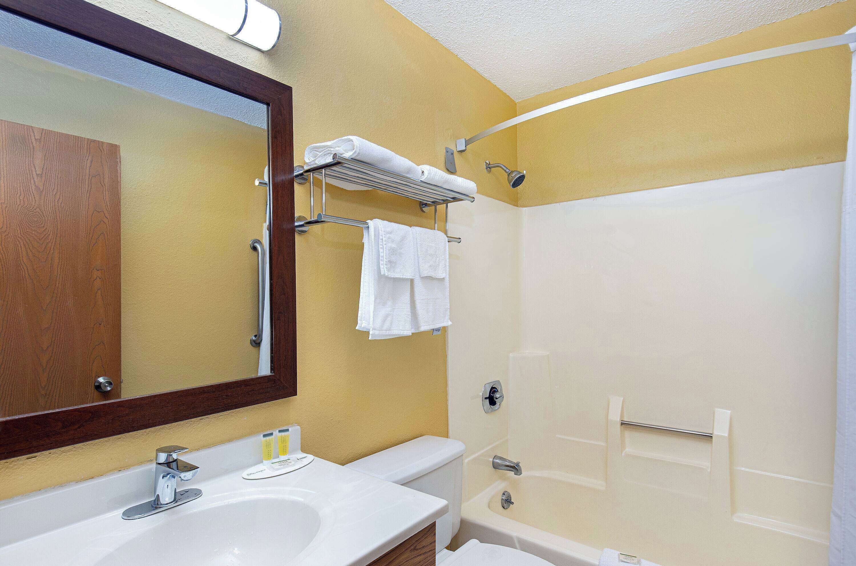 Un baño con lavamanos, espejo, toallero y ducha.