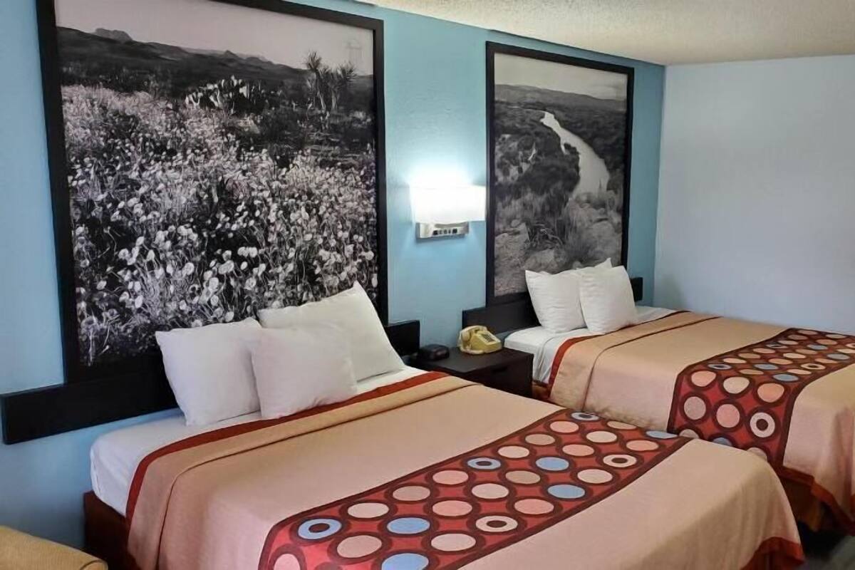 Habitación de hotel con dos camas, una mesita de noche, un escritorio y dos grandes cuadros en blanco y negro con paisajes en las paredes.