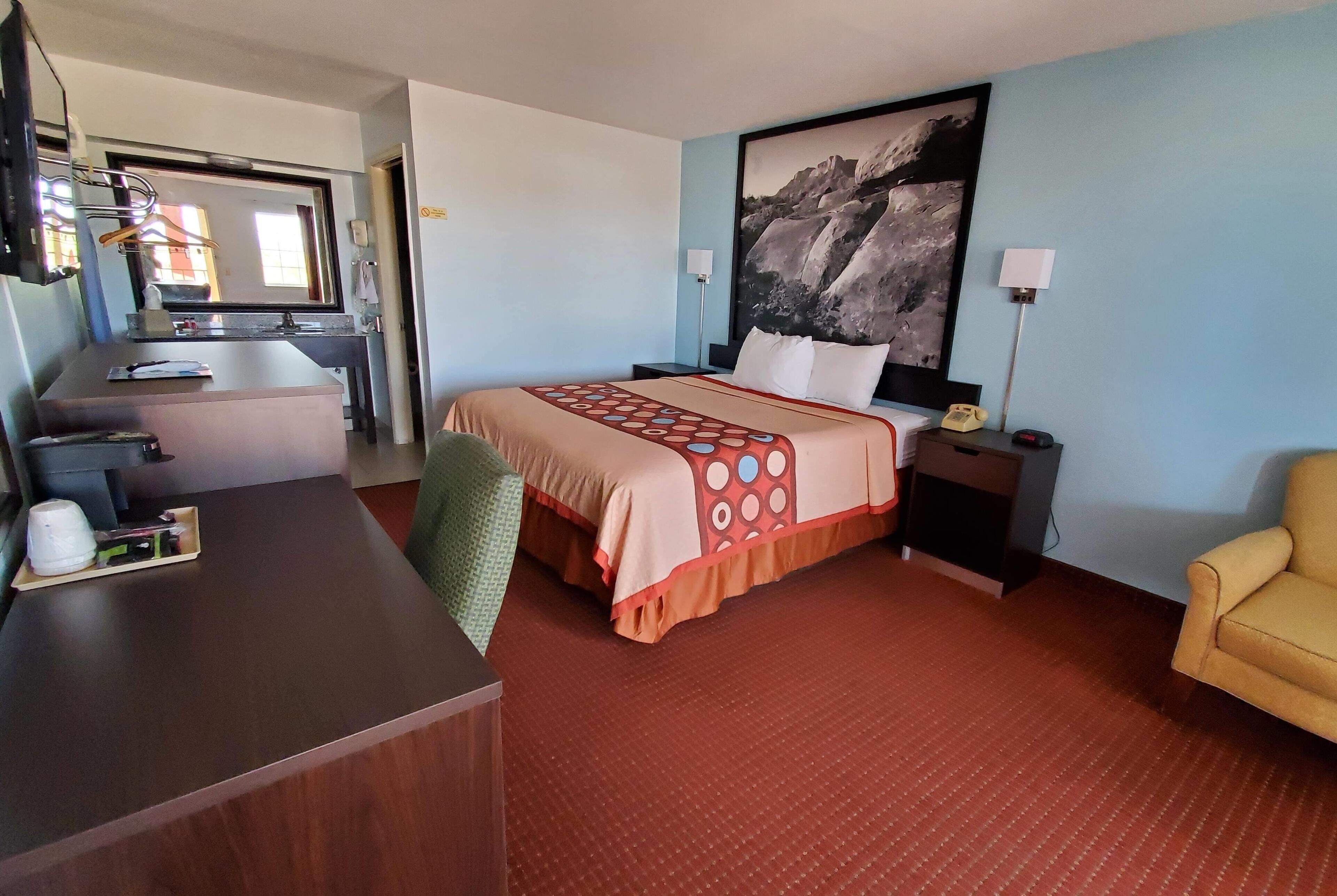 Habitación de hotel con cama, escritorio, silla y un cuadro en la pared.