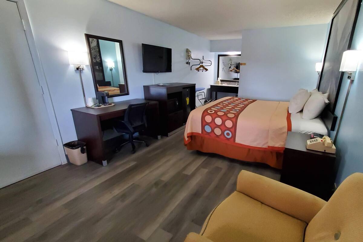 Una habitación de hotel con cama, escritorio, silla, televisión y un cubo de basura.
