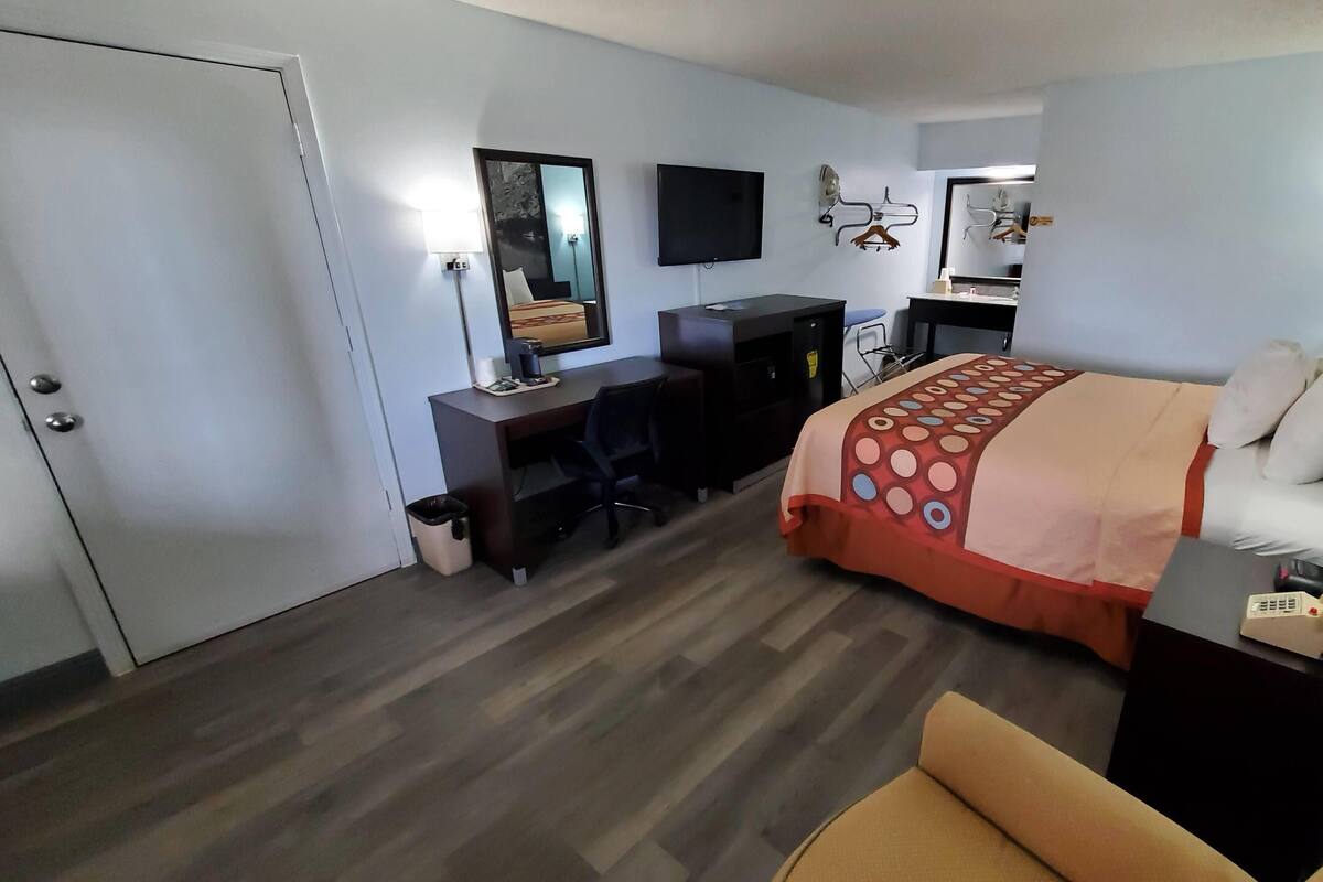 Habitación de hotel con cama, escritorio, silla, televisor y espejo.