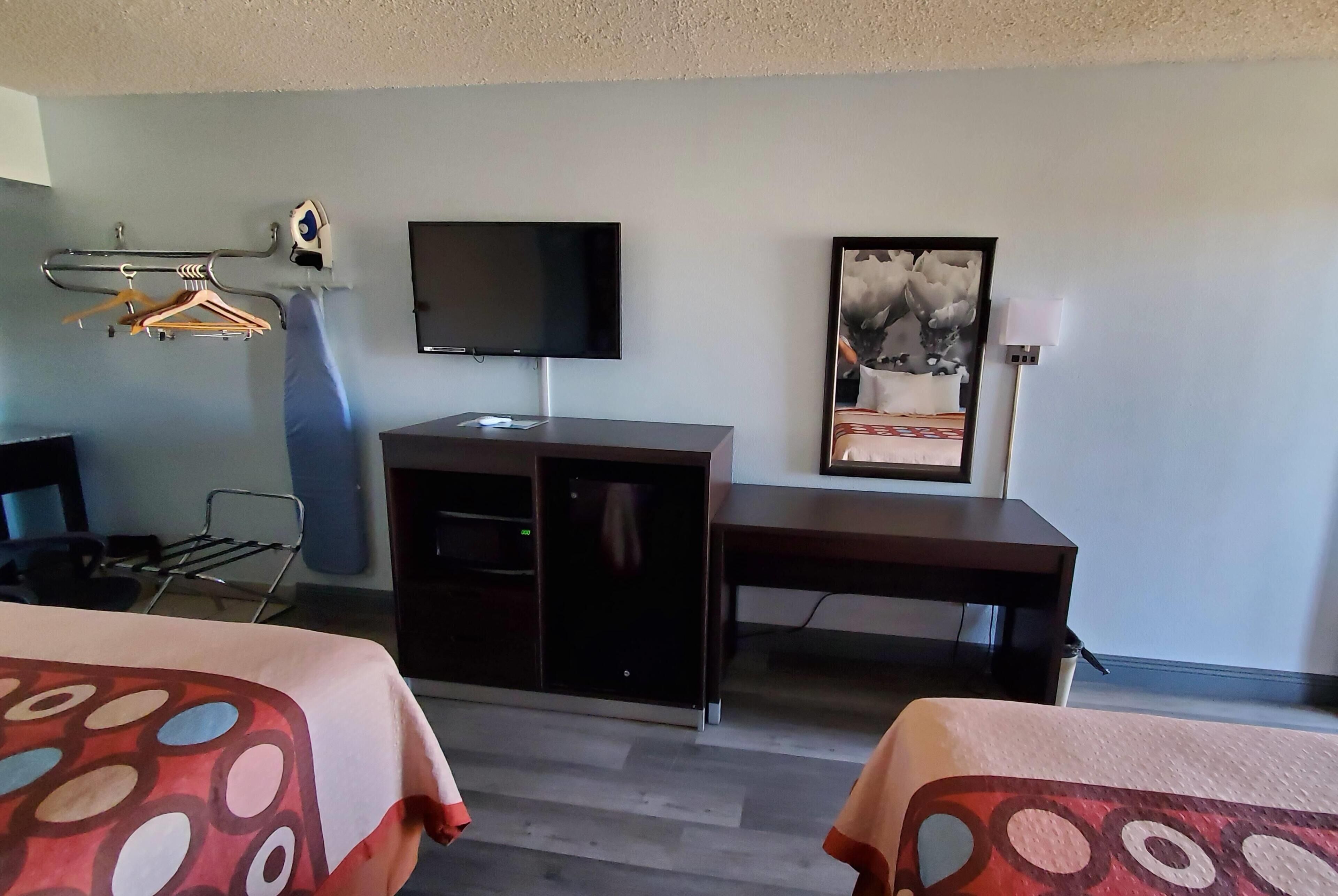 Habitación de hotel con cama, escritorio, televisión, perchero y un cuadro en la pared.