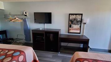 Habitación de hotel con cama, escritorio, televisión, perchero y un cuadro en la pared.