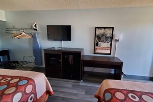 Habitación de hotel con cama, escritorio, televisión, perchero y un cuadro en la pared.