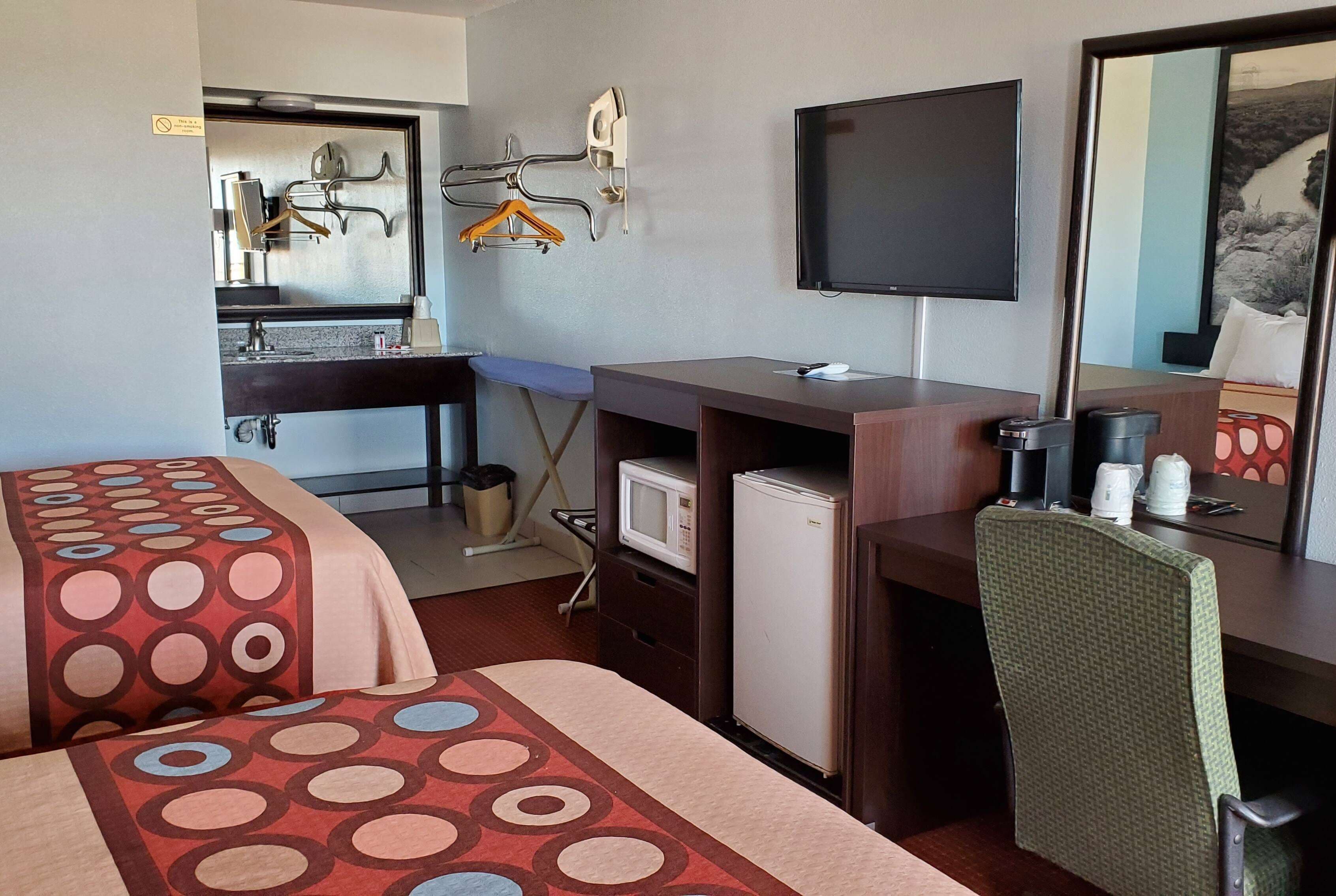 A hotel room with two beds, a desk with a computer, a television, and a microwave.