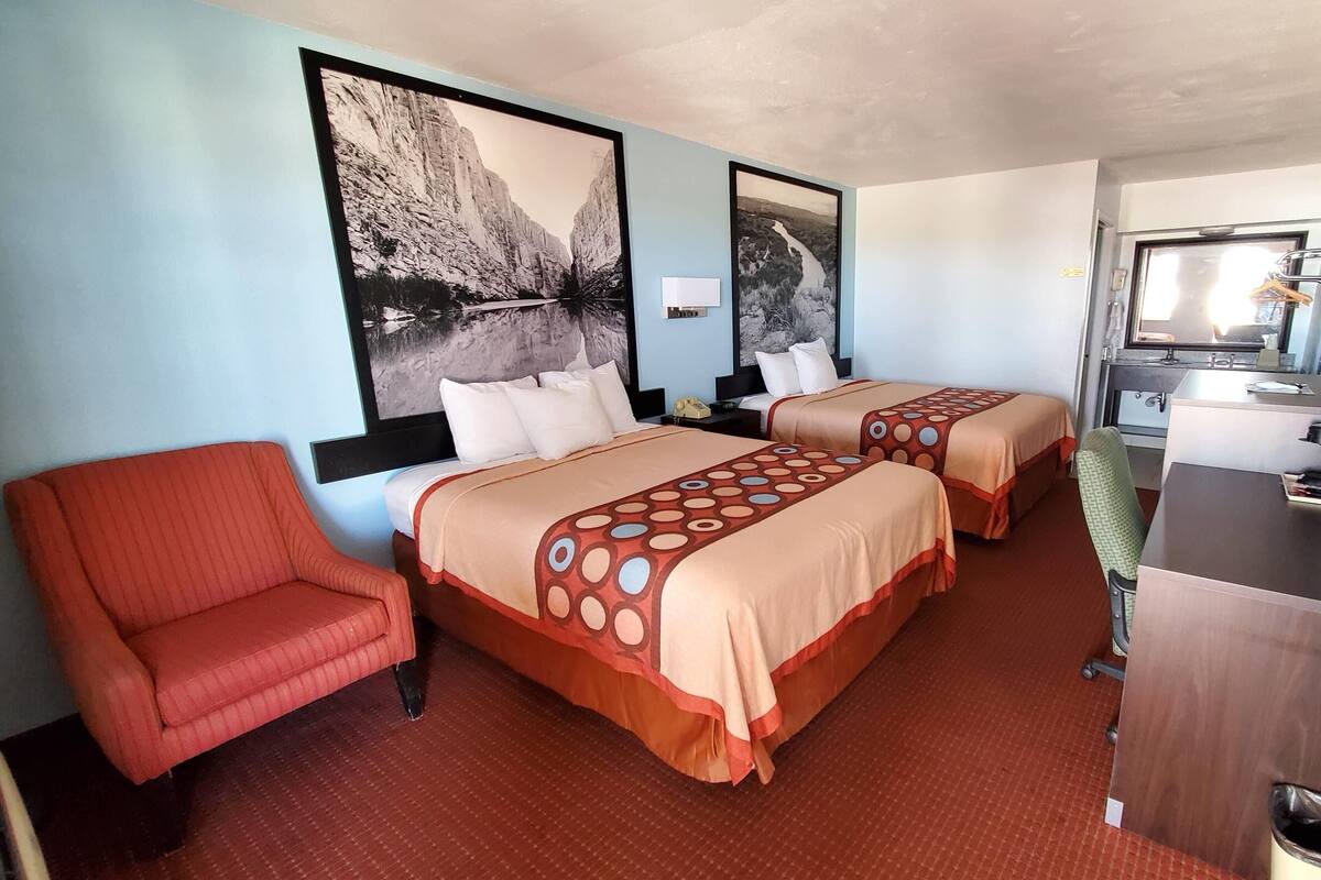 Habitación de hotel con dos camas, un sillón rojo, un escritorio y un espejo.