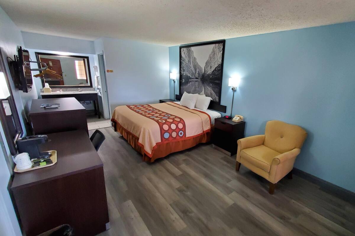 Habitación de hotel con cama, escritorio, silla, mesita de noche y un cuadro grande en la pared.