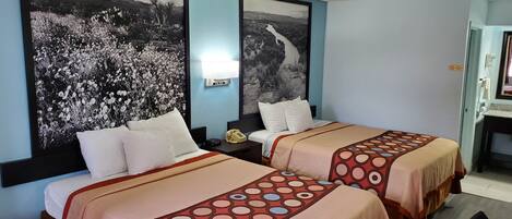 A hotel room with two beds, each with a patterned bedspread, a nightstand with a telephone, and two large framed pictures on the wall.