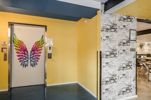 A hallway with a door featuring a colorful feather design, a wall with a brick pattern, and a sign indicating complimentary breakfast hours. - Clarion Pointe Tallahassee-State Capitol (Tallahassee)
