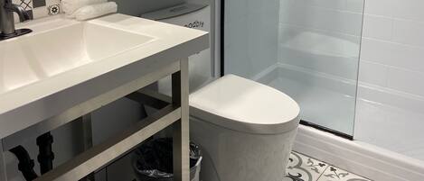 A modern bathroom with a white sink, a glass shower enclosure, and patterned floor tiles.