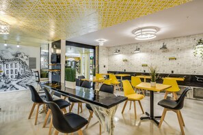 A modern dining area with a glass-top table, yellow chairs, and a patterned ceiling.