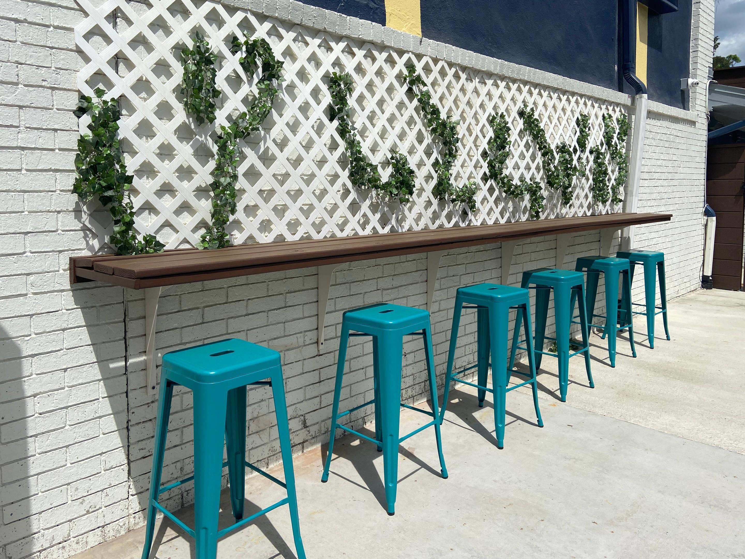 A bar area with a white lattice wall, green vines, and teal bar stools.