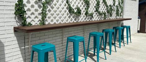 A bar area with a white lattice wall, green vines, and teal bar stools.