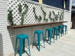 A bar area with a white lattice wall, green vines, and teal bar stools. - Clarion Pointe Tallahassee-State Capitol (Tallahassee)