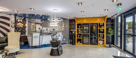 A hotel lobby with a reception desk, a wall of vinyl records, a unique sculpture, and a minibar.