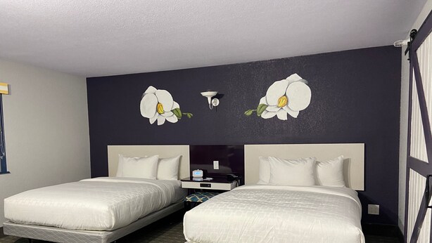 Habitación de hotel con dos camas, una mesita de noche, una lámpara y una obra de arte colgada en la pared.