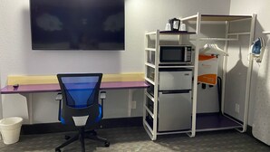 A compact room with a desk, a chair, a microwave, a refrigerator, and a small shelf unit. - Clarion Pointe Tallahassee-State Capitol (Tallahassee)