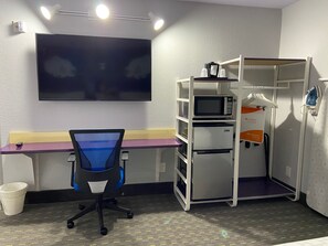 A compact room with a desk, a chair, a microwave, a refrigerator, and a small shelf unit. - Clarion Pointe Tallahassee-State Capitol (Tallahassee)