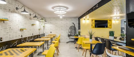 Un interior de restaurante moderno con una pared estampada, sillas amarillas y negras, y una mesa de comedor central.