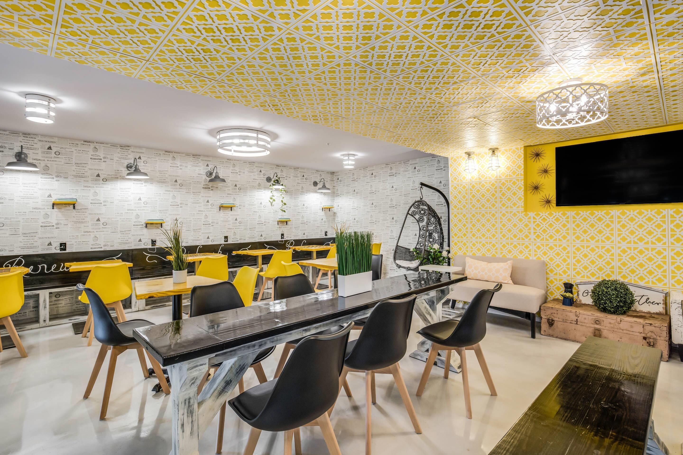 Un intérieur moderne avec un plafond à motifs, une table à manger centrale, des chaises jaunes et un canapé.