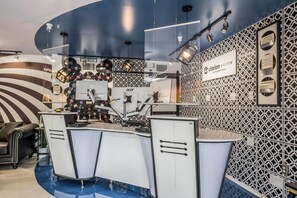 A modern hotel reception area with a curved counter, a music-themed wall, and a patterned wall with hotel signage. - Clarion Pointe Tallahassee-State Capitol (Tallahassee)